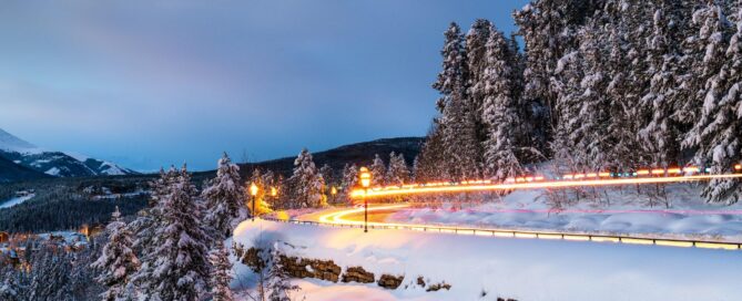 Snow-covered road winding through trees in Breckenridge, Colorado, featuring winter scenery and illuminated light trails, ideal for skiing and outdoor activities.