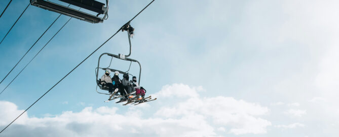 Skiers on a lift chair at Beaver Creek Ski Resort against a cloudy sky, highlighting the resort's skiing experience and amenities.