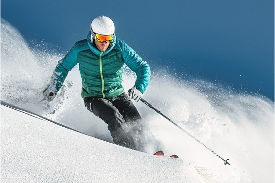 Skier in a teal jacket and helmet carving through fresh snow against a clear blue sky.