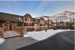 Exterior view of a ski rental lodge with flags, snow-covered ground, and mountainous backdrop in Colorado, emphasizing winter sports accessibility.