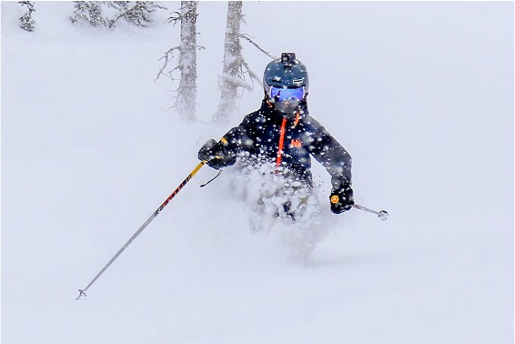 Skier navigating through deep powder snow, wearing a helmet and goggles, with snowflakes flying around.