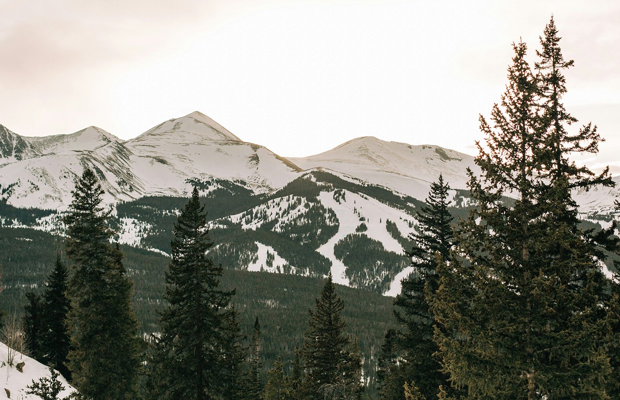 Snow-covered mountains in Breckenridge, Colorado, surrounded by evergreen trees, showcasing winter sports terrain ideal for skiing and snowboarding rentals.