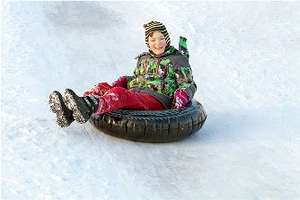 Child in colorful winter attire enjoying tubing on snow at Beaver Creek, highlighting winter activities near ski resort.