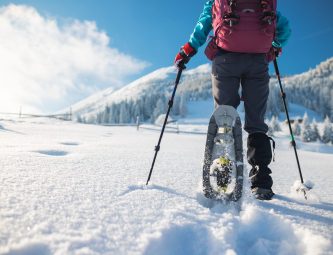Person snowshoeing in snowy landscape with adjustable poles, showcasing winter outdoor activity and snowshoe rental options.