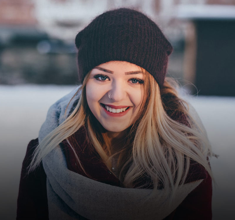 Smiling young woman in winter attire, wearing a dark beanie and scarf, representing the friendly and knowledgeable team at Charter Sports for outdoor rental services.