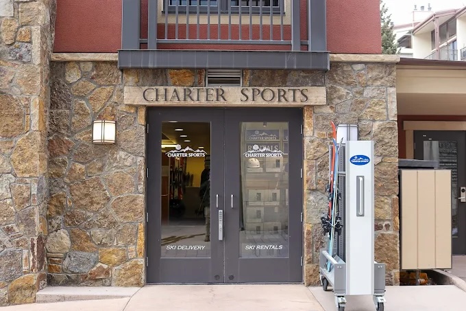 Charter Sports entrance at Lion Square Lodge North featuring ski rental and delivery services, with a stone facade and ski equipment display.