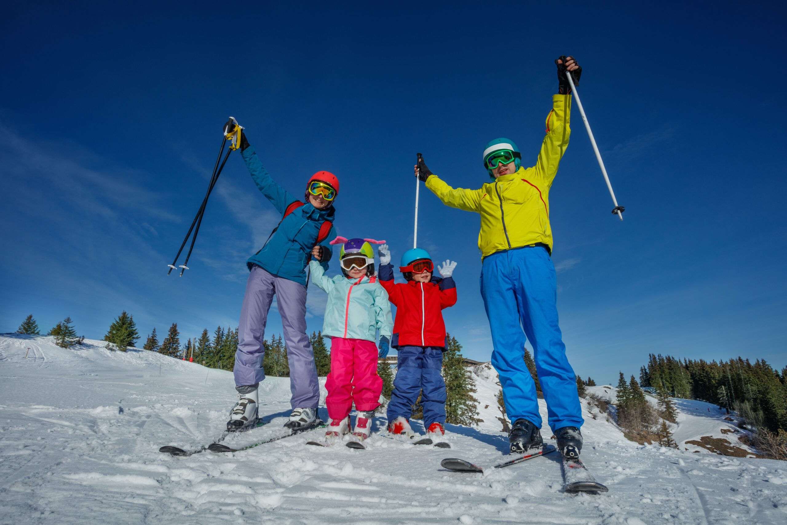 Family of four enjoying skiing on snow-covered slopes, wearing colorful winter gear and ski equipment, showcasing excitement and readiness for winter sports.