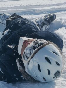 Skier lying in snow, wearing a helmet and snow gear, illustrating the challenges of skiing in variable conditions at Copper Mountain.